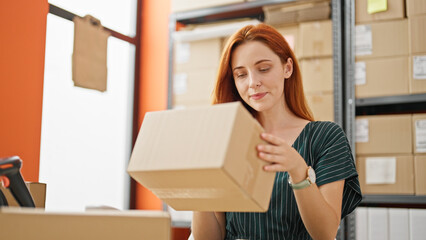 Young redhead woman ecommerce business worker holding package sitting on table at office