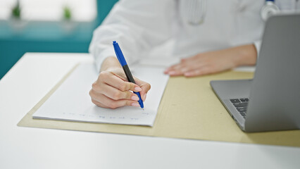 Young redhead woman doctor using laptop writing medical report at clinic