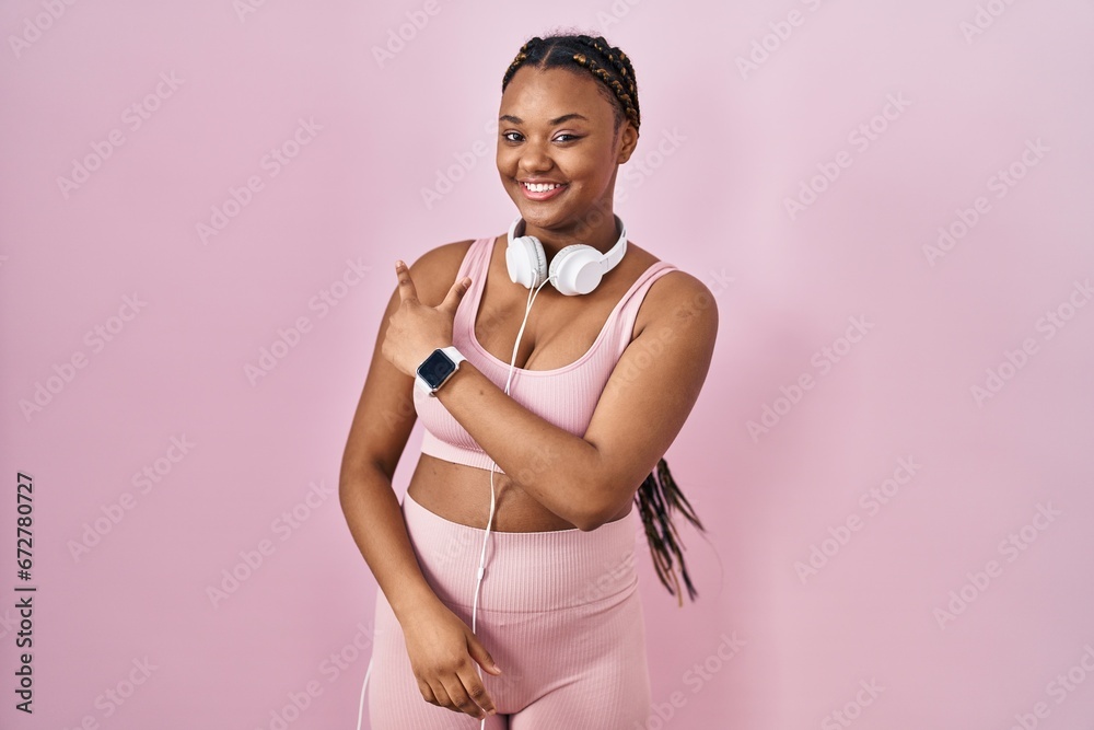 Sticker African american woman with braids wearing sportswear and headphones cheerful with a smile on face pointing with hand and finger up to the side with happy and natural expression