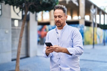 Young caucasian man using smartphone with serious expression at street