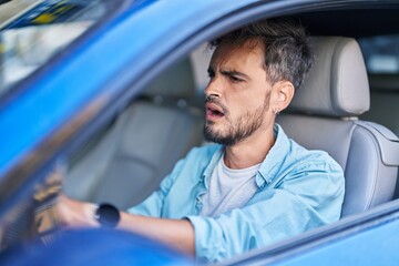 Young hispanic man stressed driving car at street