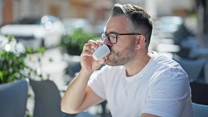 Grey-haired man drinking coffee sitting on table at coffee shop terrace