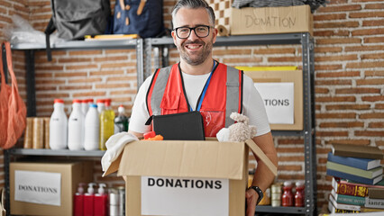Grey-haired man volunteer wearing vest holding donations package at charity center
