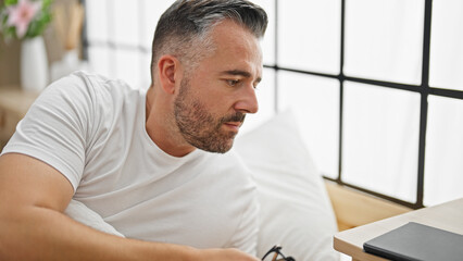 Grey-haired man lying on bed with serious expression at bedroom