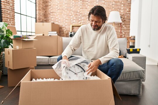 Middle age man smiling confident unpacking cardboard box at new home