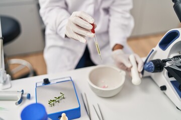 Young beautiful hispanic woman scientist pouring liquid on bowl at laboratory