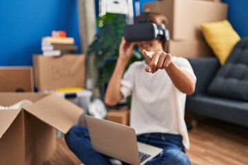 Young beautiful hispanic woman playing video game using virtual reality glasses sitting on floor at...