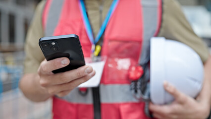 Young caucasian man architect using smartphone holding hardhat at construction place
