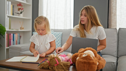 Caucasian mother & little daughter opening laptop to draw on notebook, sitting at home, smiling and relaxing together on living room sofa