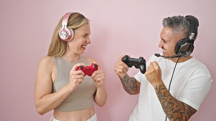 Man and woman couple playing video game smiling over isolated pink background