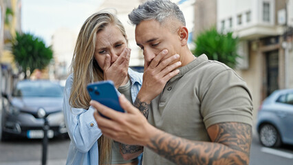 Man and woman couple using smartphone looking upset at street