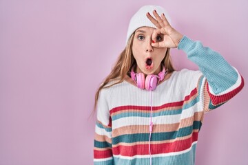 Young blonde woman standing over pink background doing ok gesture shocked with surprised face, eye looking through fingers. unbelieving expression.