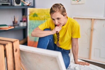 Young blonde woman artist looking draw with serious expression at art studio