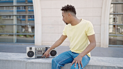 African american man turning boombox on sitting on bench at street