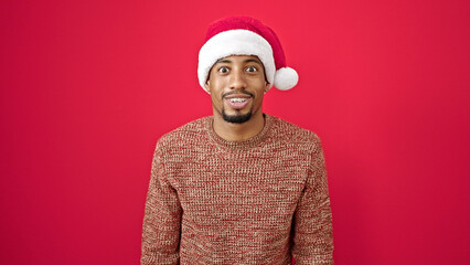 African american man surprise expression wearing christmas hat over isolated red background