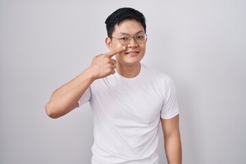 Young asian man standing over white background pointing with hand finger to face and nose, smiling cheerful. beauty concept