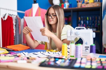 Fototapeta premium Young beautiful hispanic woman tailor reading document at clothing factory