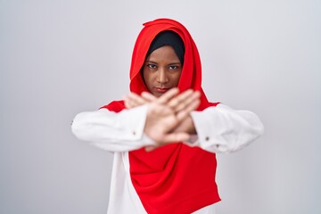 Young arab woman wearing traditional islamic hijab scarf rejection expression crossing arms and...