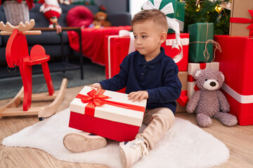 Obraz na płótnie Canvas Adorable hispanic boy unpacking gift sitting by christmas tree at home