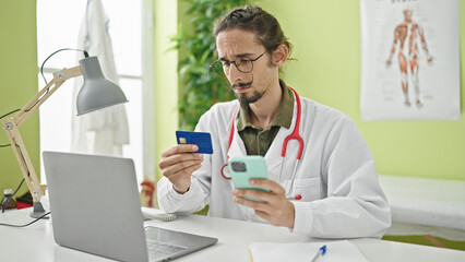 Young hispanic man doctor shopping with smartphone and credit card at clinic
