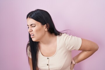 Young hispanic woman standing over pink background suffering of backache, touching back with hand, muscular pain