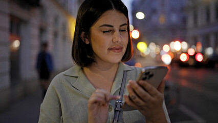 Fototapeta premium Young beautiful hispanic woman using smartphone in the streets at night