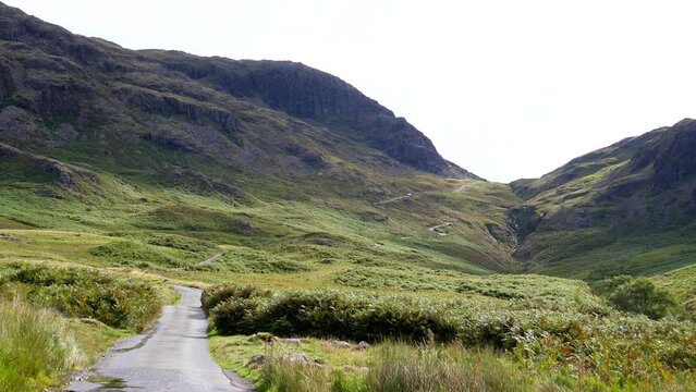 Motorcycle reaching the top of mountain pass, car driving down winding single lane road from Hard Knott Pass Hardknott Pass to Eskdale in Lake District, England, UK.