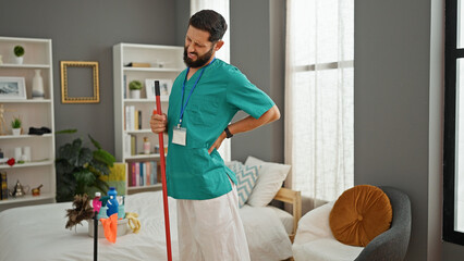 Young hispanic man professional cleaner cleaning floor suffering for backache at bedroom