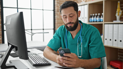 Young hispanic man doctor using smartphone at the clinic