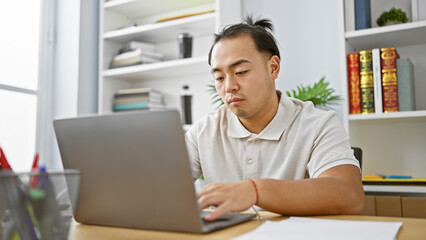 Serious young chinese man, a focused business professional, immersing in work with his laptop at...