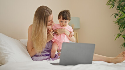 Mother and daughter using laptop sitting on bed at bedroom