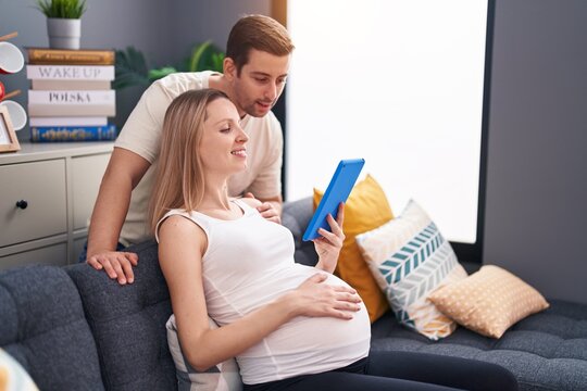 Man and woman couple using touchpad expecting baby at home - Powered by Adobe