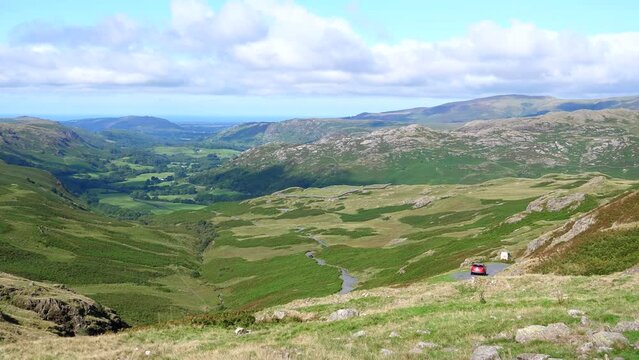 Looking down to Eskdale valley in Lake District National Park, UK. Minibus struggling to make a sharp turn on narrow mountain road.