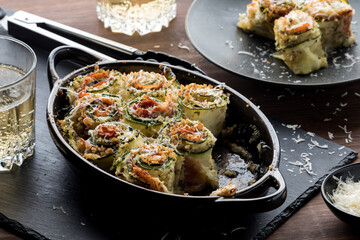 Hot zucchini rollups with a serving in behind, topped with parmesan cheese.