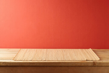 Empty wooden table with bamboo place mat  over red background. Chinese New Year mock up for design and product display.