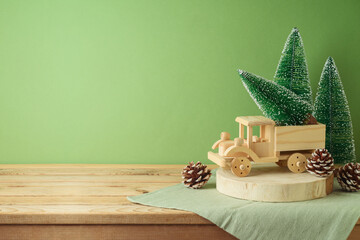 Wooden table with pine tree decoration and toy truck over green background.  Christmas and winter...