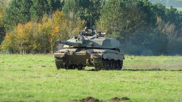 Commander and gunner directing a British army FV4034 Challenger 2 ii main battle tank moving across a grass field at speed, on a military exercise, Wiltshire UK