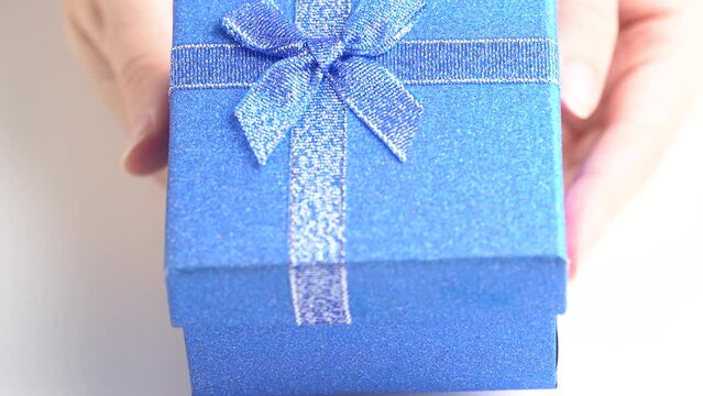 Hands put a gift box on the table, presented with a gift. Glittering blue gift box, close up. Gift concept or birthday party.
