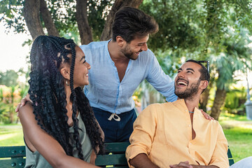 Fototapeta premium Three friends of diverse ethnicities share a joyous moment, laughing together on a sunny day in the park, epitomizing casual friendship.