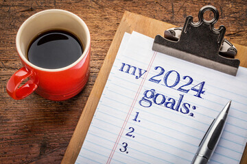 my 2024 goals list on clipboard and coffee against grunge wood desk, setting New Year goals and resolutions - 672805503