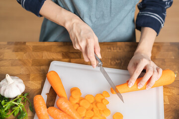 Asian young woman, girl or housewife hand using knife, cutting carrots on  board, on wooden table in kitchen home, preparing ingredient, recipe fresh vegetables for cooking meal. Healthy food people.
