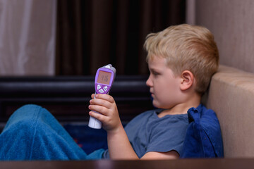 Sick little boy measures temperature, lies in bed at home. The child has a high temperature. Flu