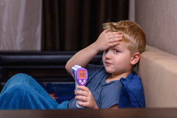 Sick little boy measures temperature, lies in bed at home. The child has a high temperature. Flu