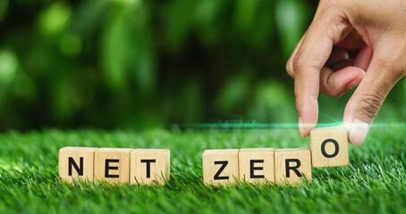 Hand puts wooden cubes for net zero emissions concept on the grass with green...