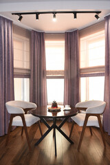 The room is cozy with curtains and a window with a table chairs and tea on the table