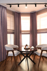 The room is cozy with curtains and a window with a table chairs and tea on the table