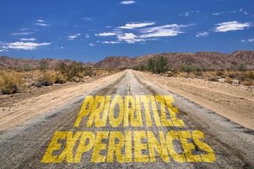 A road winding through a rural landscape, with a bright yellow sign reading Prioritize Experiences