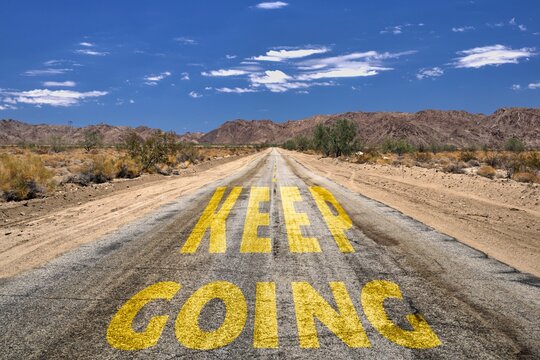 Idyllic country road winding through a rural landscape, with a bright yellow sign reading Keep going