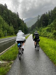 two cyclists in rain gear traveling down a road in the mountains
