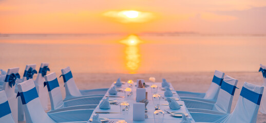 Concept of a tropical destination wedding in front of the ocean. Beautiful wedding arch on the beach. Table setting at a luxury wedding and Beautiful flowers on the table. Dream sunset decoration